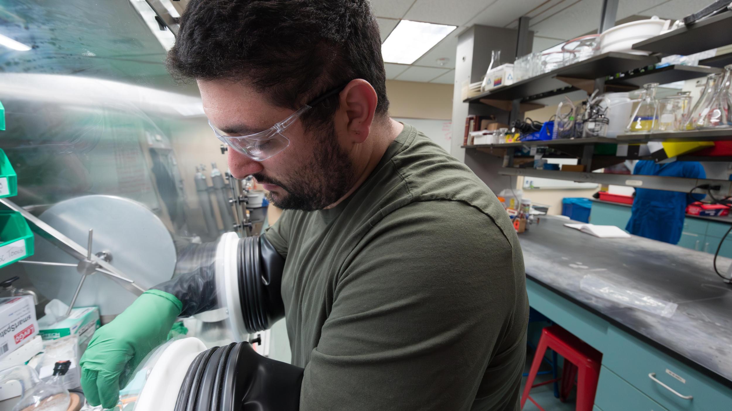 A man in a green shirt and green gloves working in a laboratory.