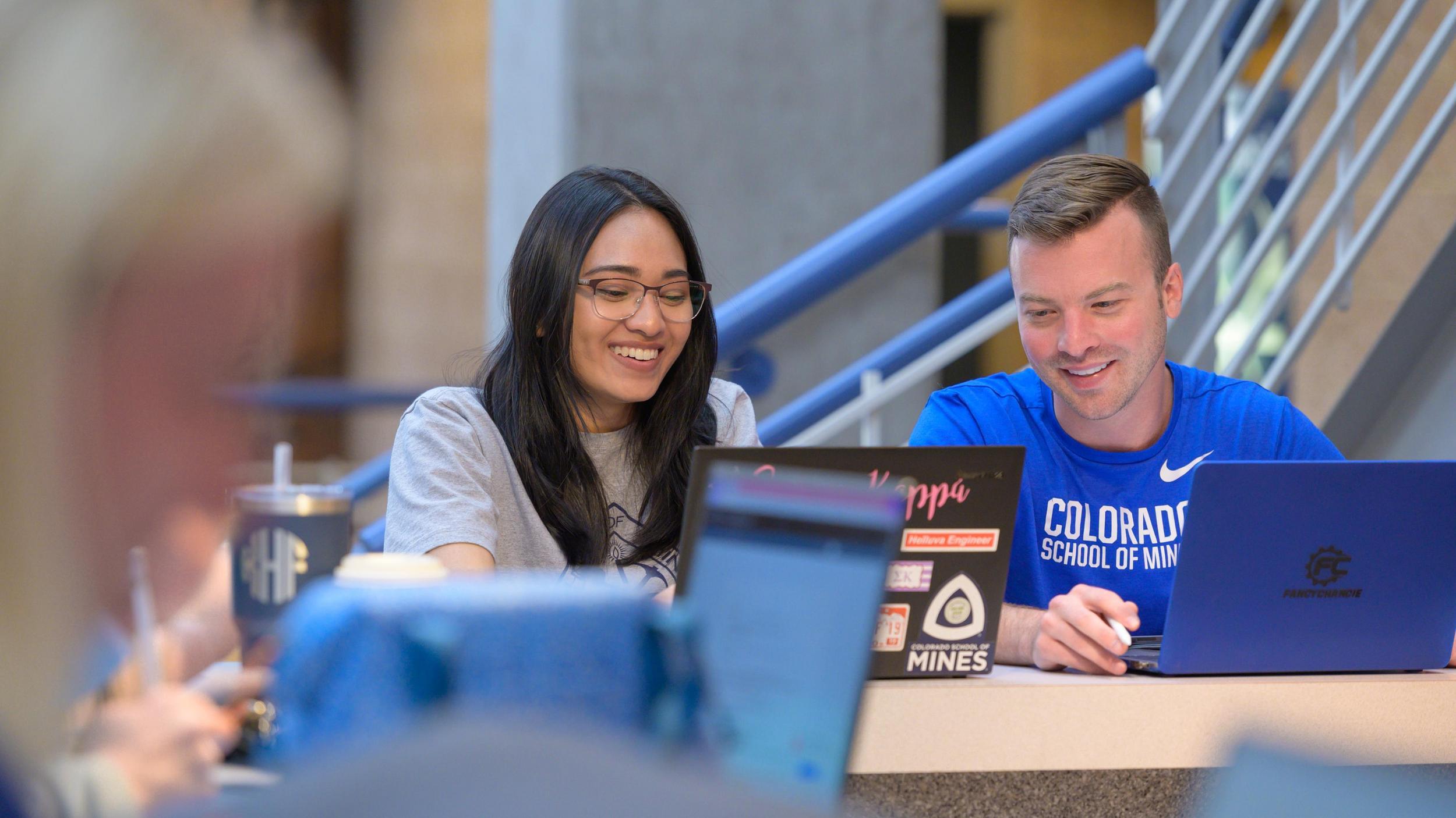 A man and a woman sitting at a table with laptops.