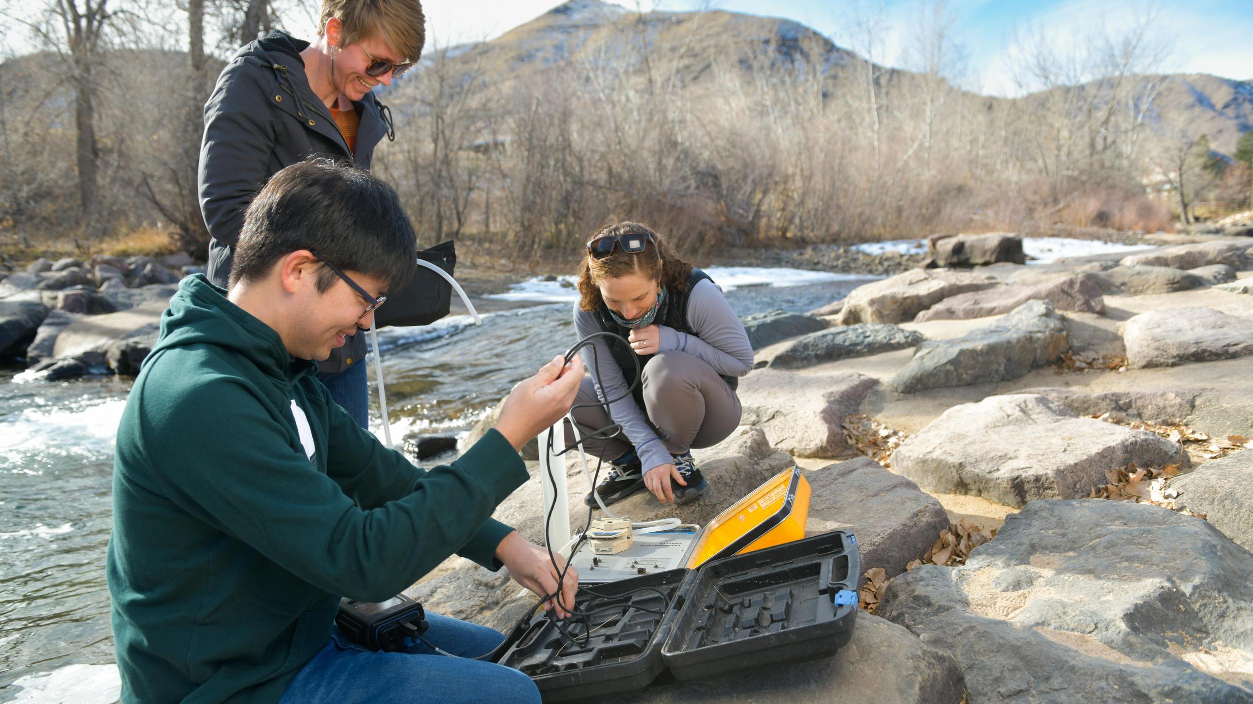 A group of people sitting on top of a rock next to a river.
